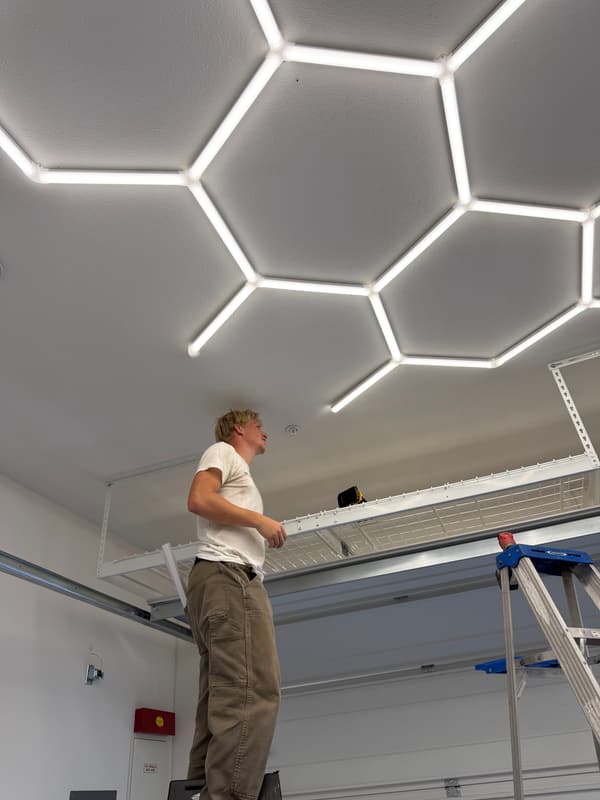 Installer on a ladder fitting a hexagon LED ceiling grid in a garage