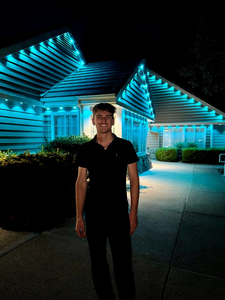 John Fox, owner of JFX Lighting, in front of a home lit in teal permanent lights