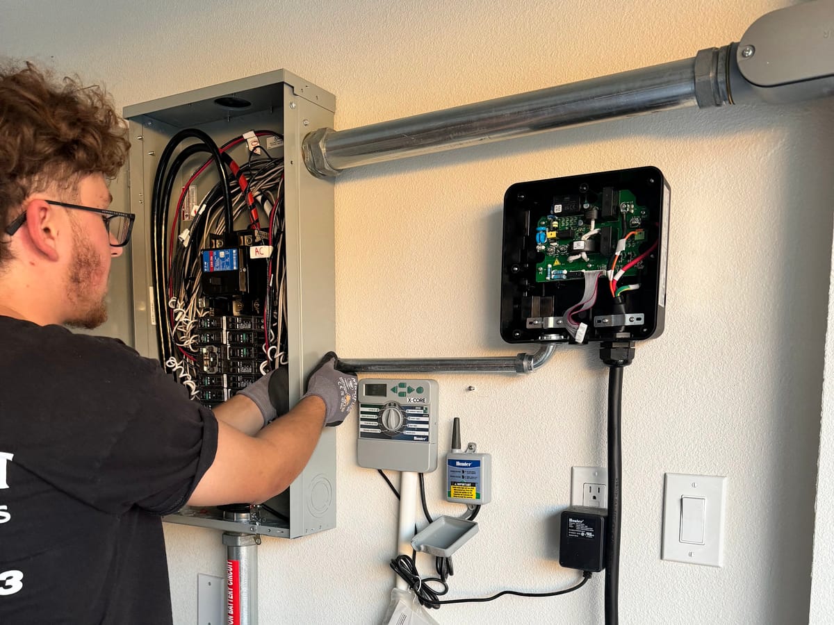 JFX Lighting electrician working inside an open electrical panel next to an EV charger install in a garage