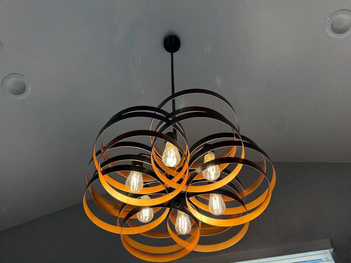 Black and gold ribbon chandelier with exposed warm bulbs hanging under a vaulted ceiling