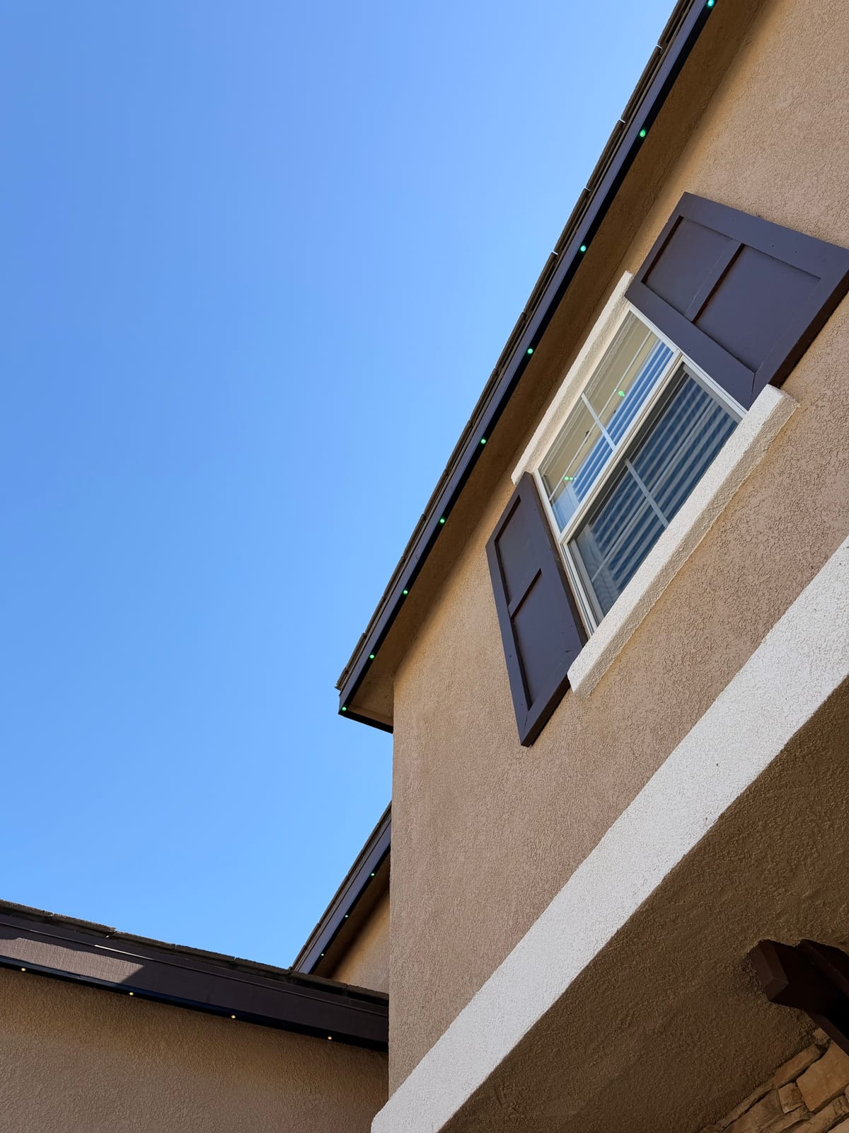 Daytime close-up of permanent lights installed in a dark track along a stucco home's fascia, barely visible against the trim