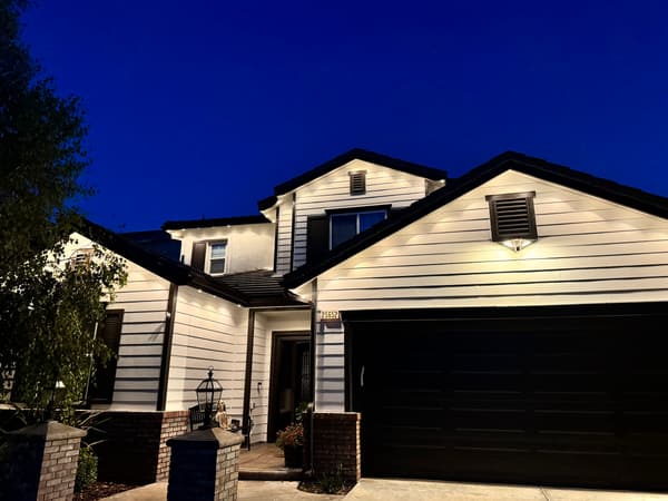White two-story home with dark trim at dusk, warm white permanent lights along the gables and over the garage