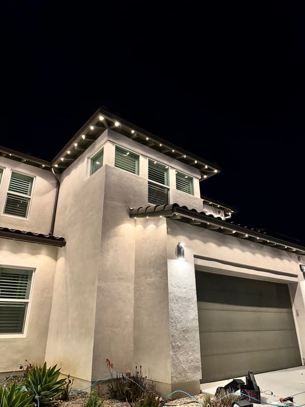 Two-story stucco home at night with warm white lights along the upper rooflines