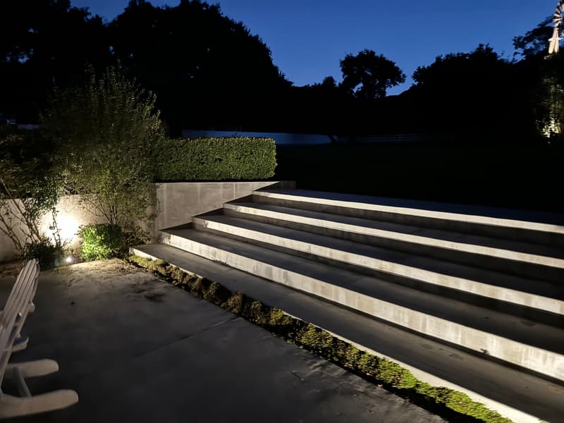Wide outdoor steps and planting beds lit with landscape lights at dusk