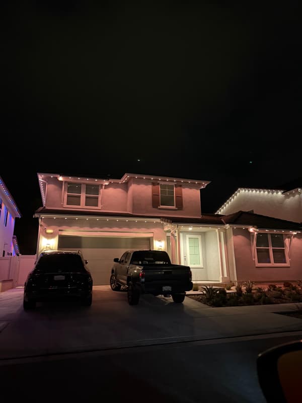 Two-story home at night with pink-tinted roofline lights