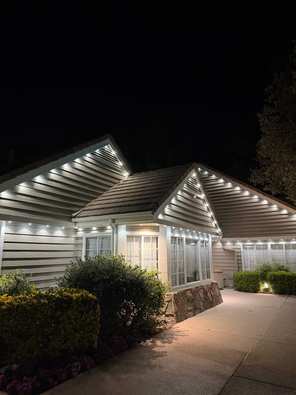 Single-story home with lap siding at night, bright white eave lights along every gable