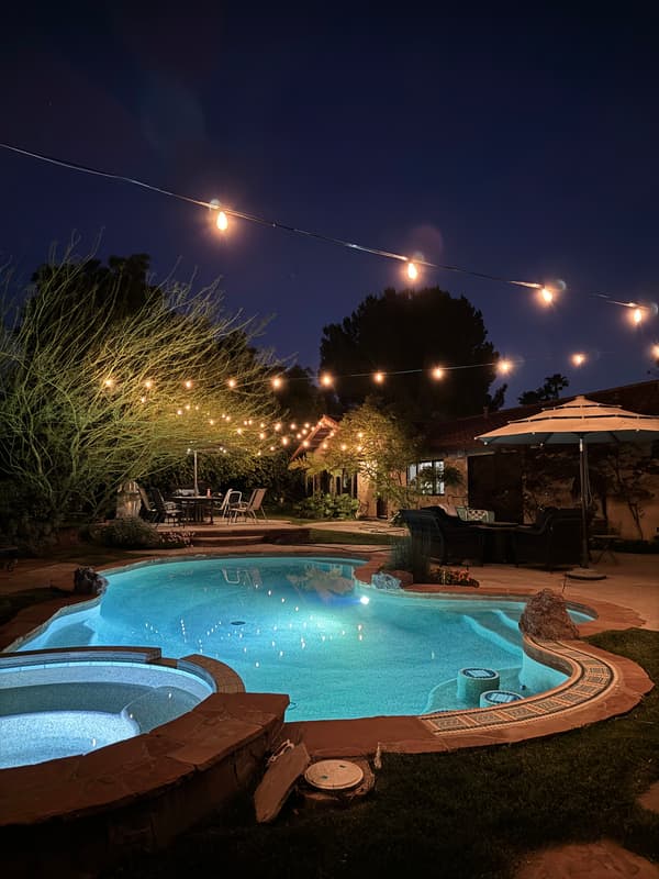 Pool and spa at night under strands of warm string lights
