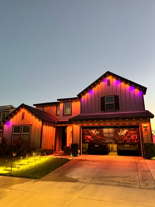 Two-story home at dusk lit in orange and purple for Halloween, with path lights along the lawn
