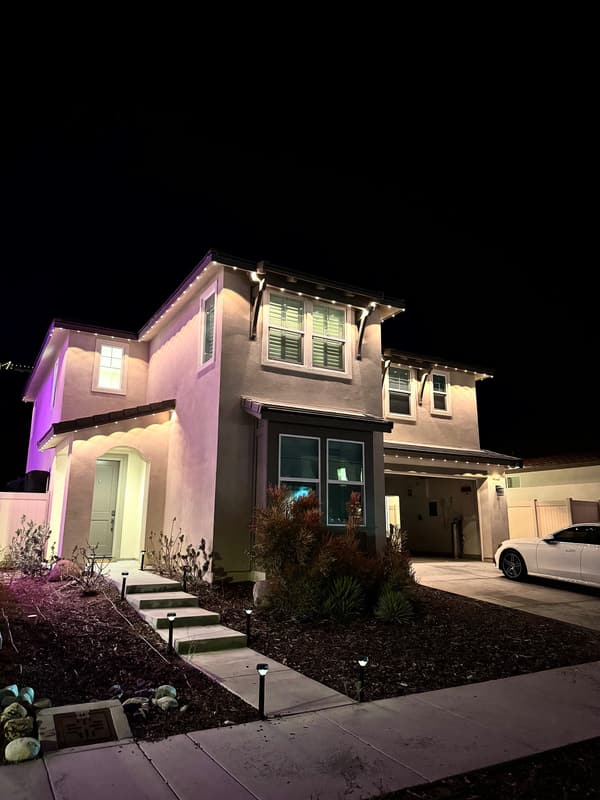 Two-story home at night with white roofline lights and a purple accent light washing the side wall